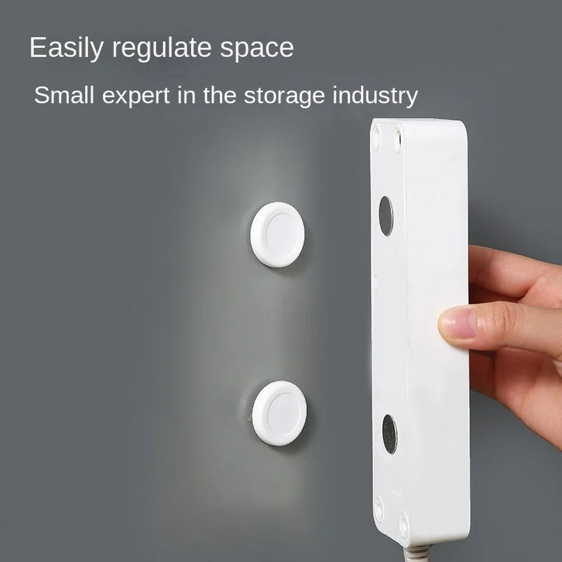 Hand holding a device near two magnetic adhesive wall mounts on a gray wall