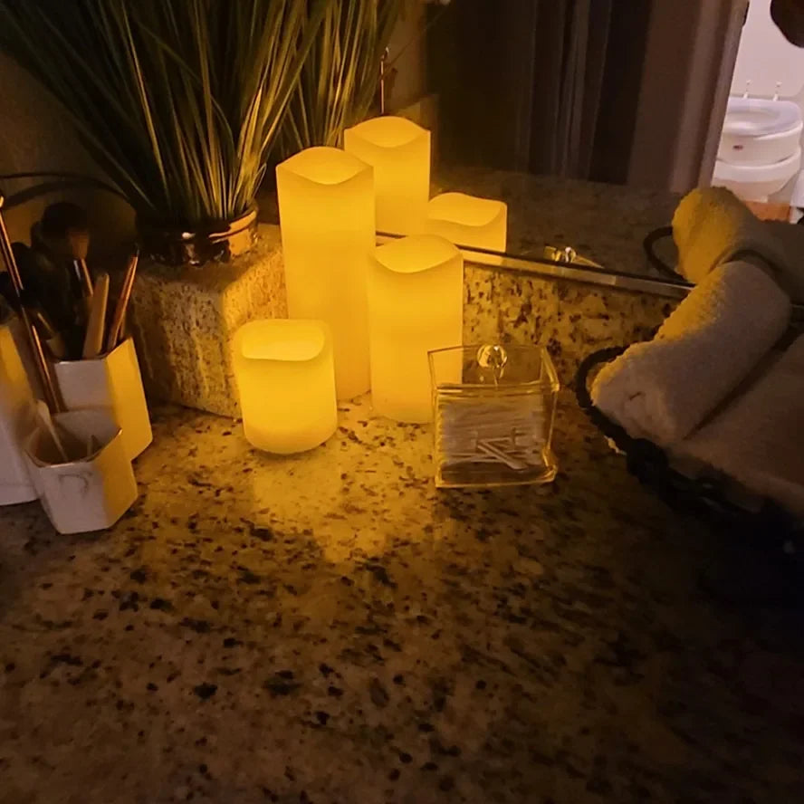 Cluster of flameless LED pillar candles creating a cozy ambiance on a bathroom countertop with towels and toiletries