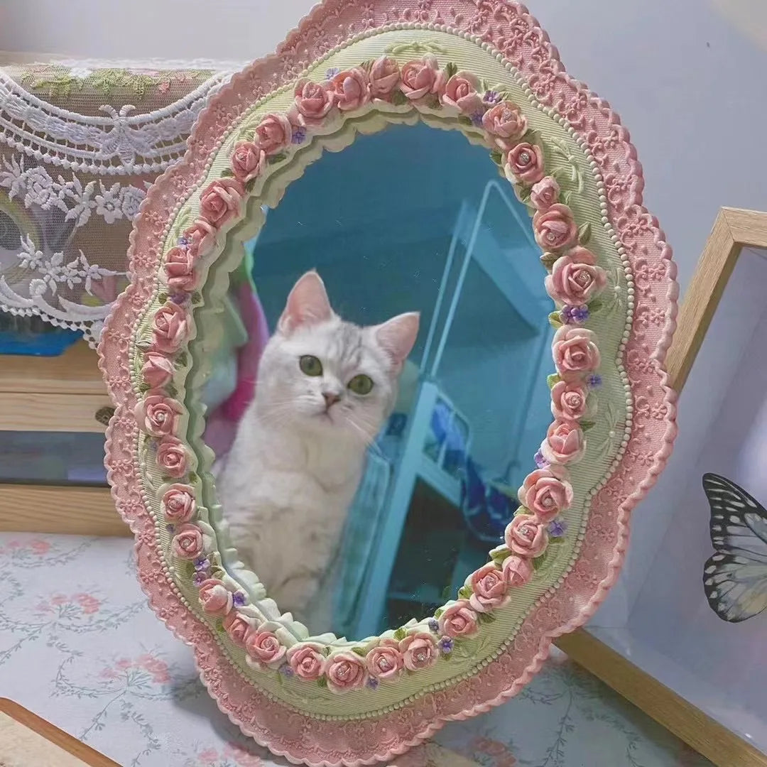 Decorative pink oval mirror with roses reflecting a white cat and floral decor