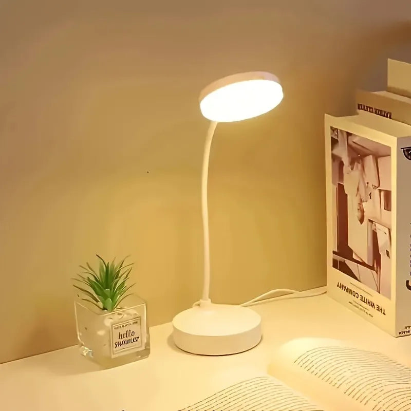 Flexible LED desk lamp with warm light on a desk beside books and a small plant