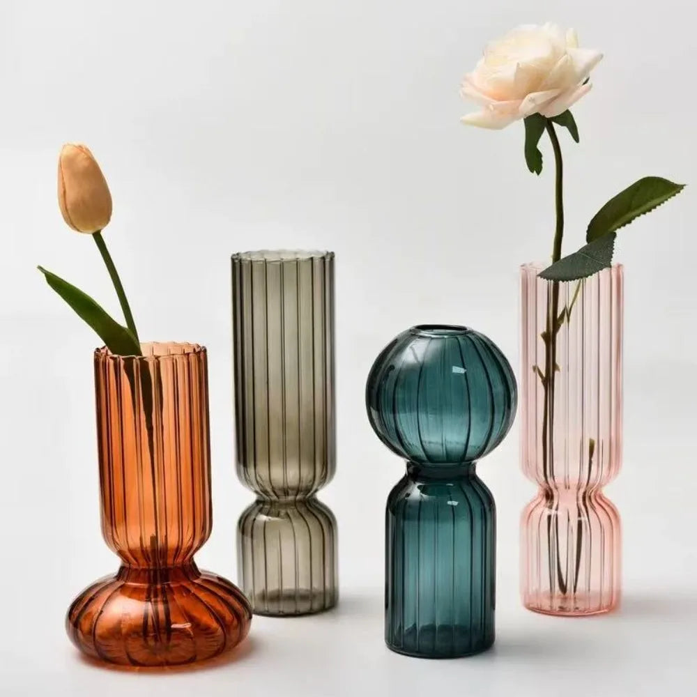 Four colorful striped glass vases in orange, smoky gray, teal, and pink, each in a distinctive modern shape