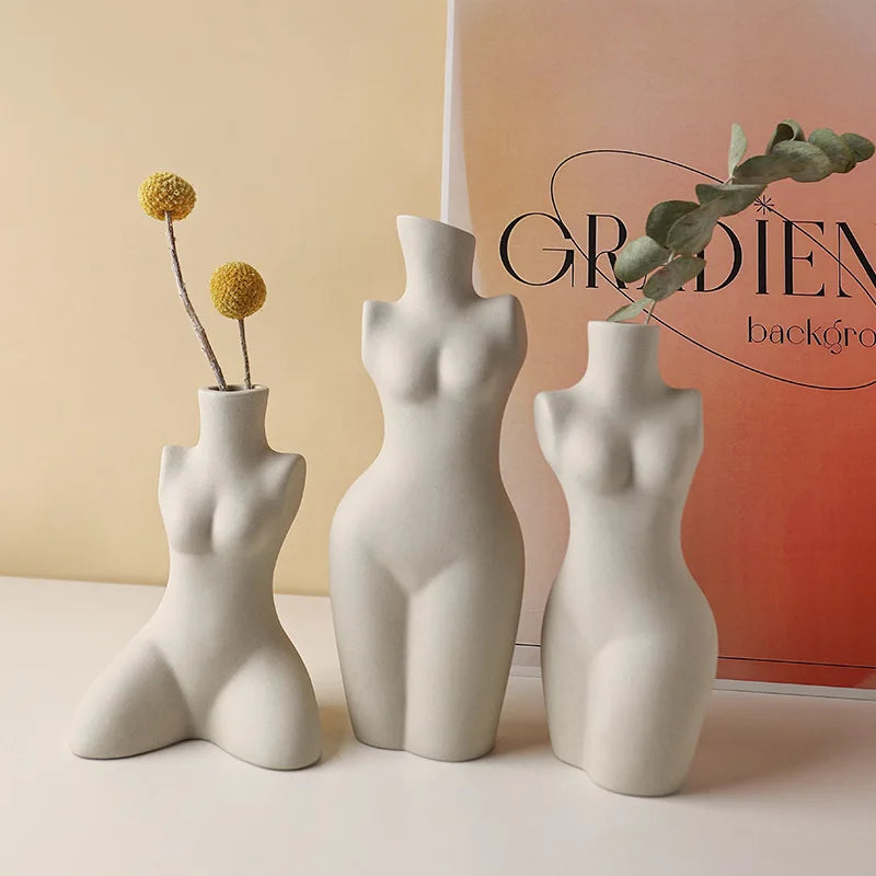 Three ceramic body sculpture vases in neutral tones on a tabletop with flowers and eucalyptus