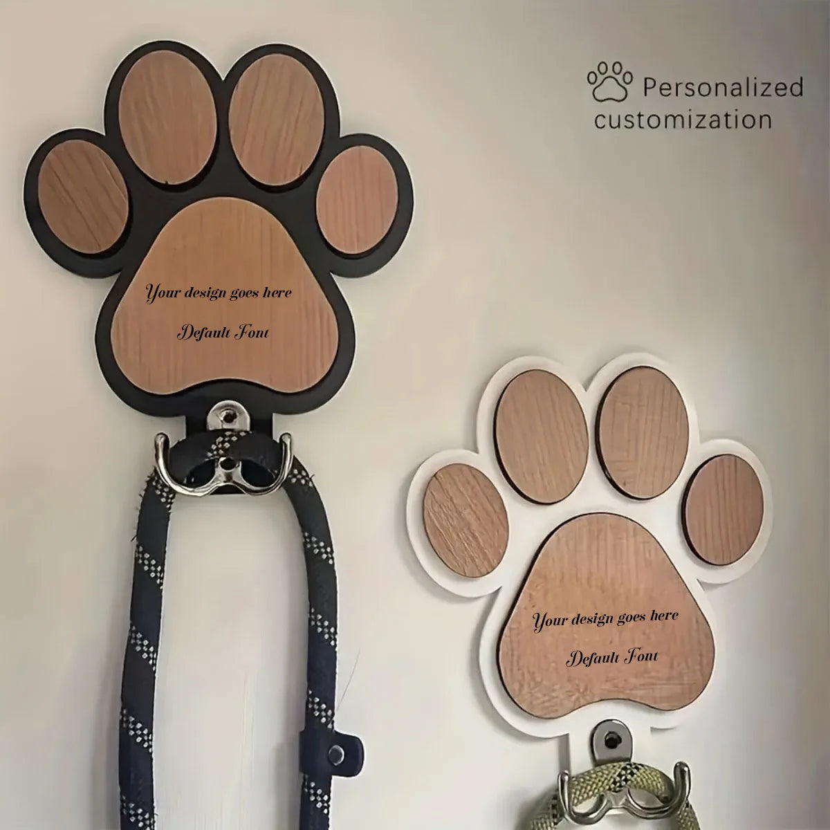 Black and white paw print wooden dog leash hooks with metal hangers, mounted on a wall, one personalized for demonstration