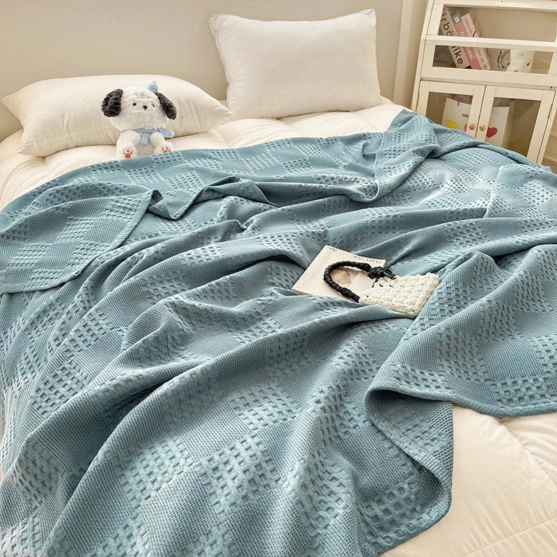 Blue cotton waffle throw blanket draped casually across bed with white pillows
