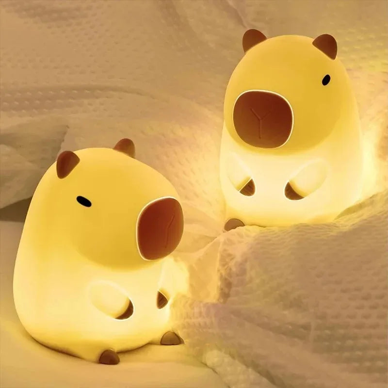 Two capybara-shaped night lights glowing softly on a bed
