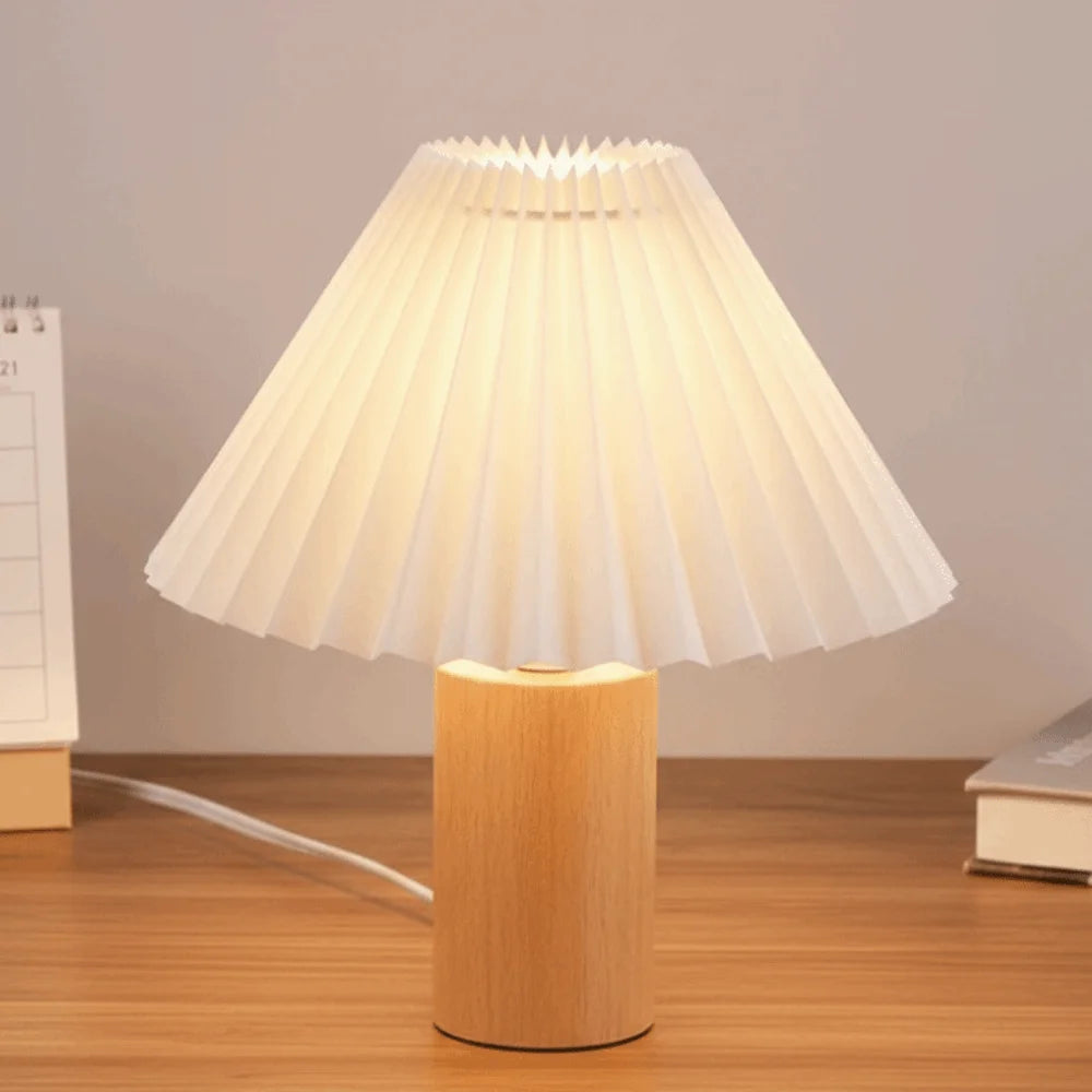 White pleated lampshade on a wooden table lamp base in a cozy room