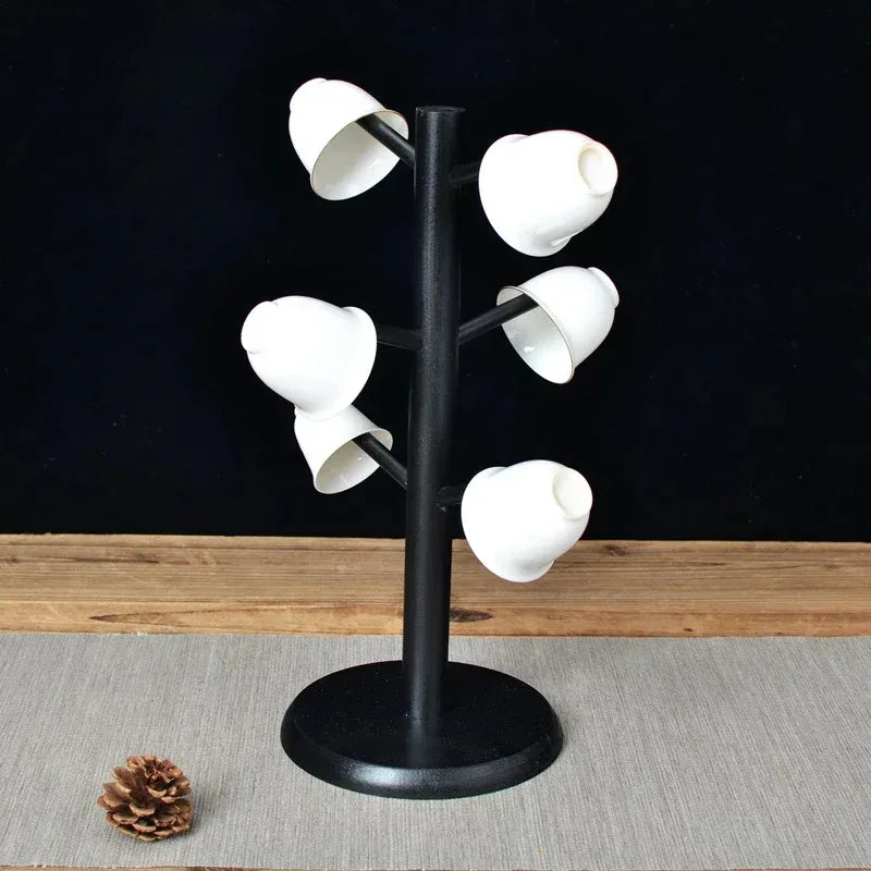 Black wooden mug tree stand holding six white cups, displayed on a wooden table.