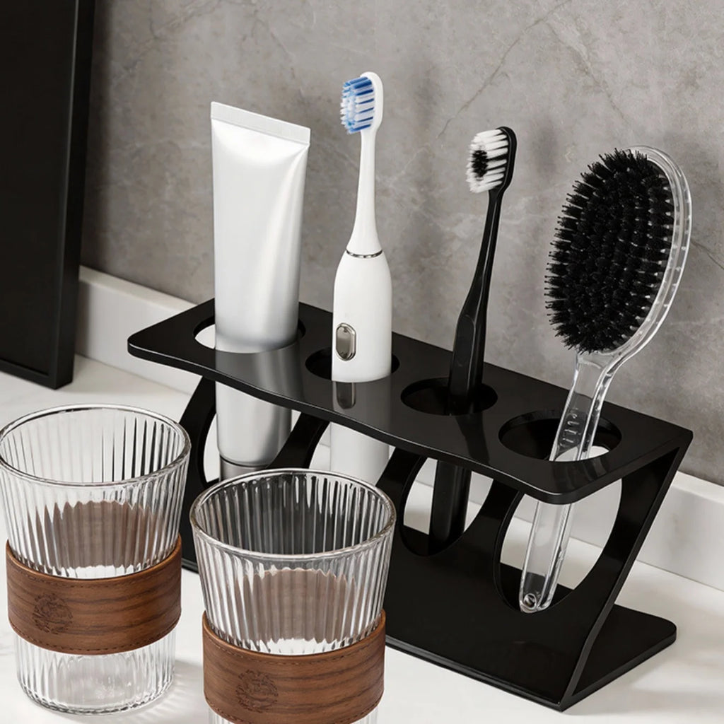 Black plastic ventilated toothbrush and toothpaste stand on bathroom counter holding brushes, toothpaste, and a small comb