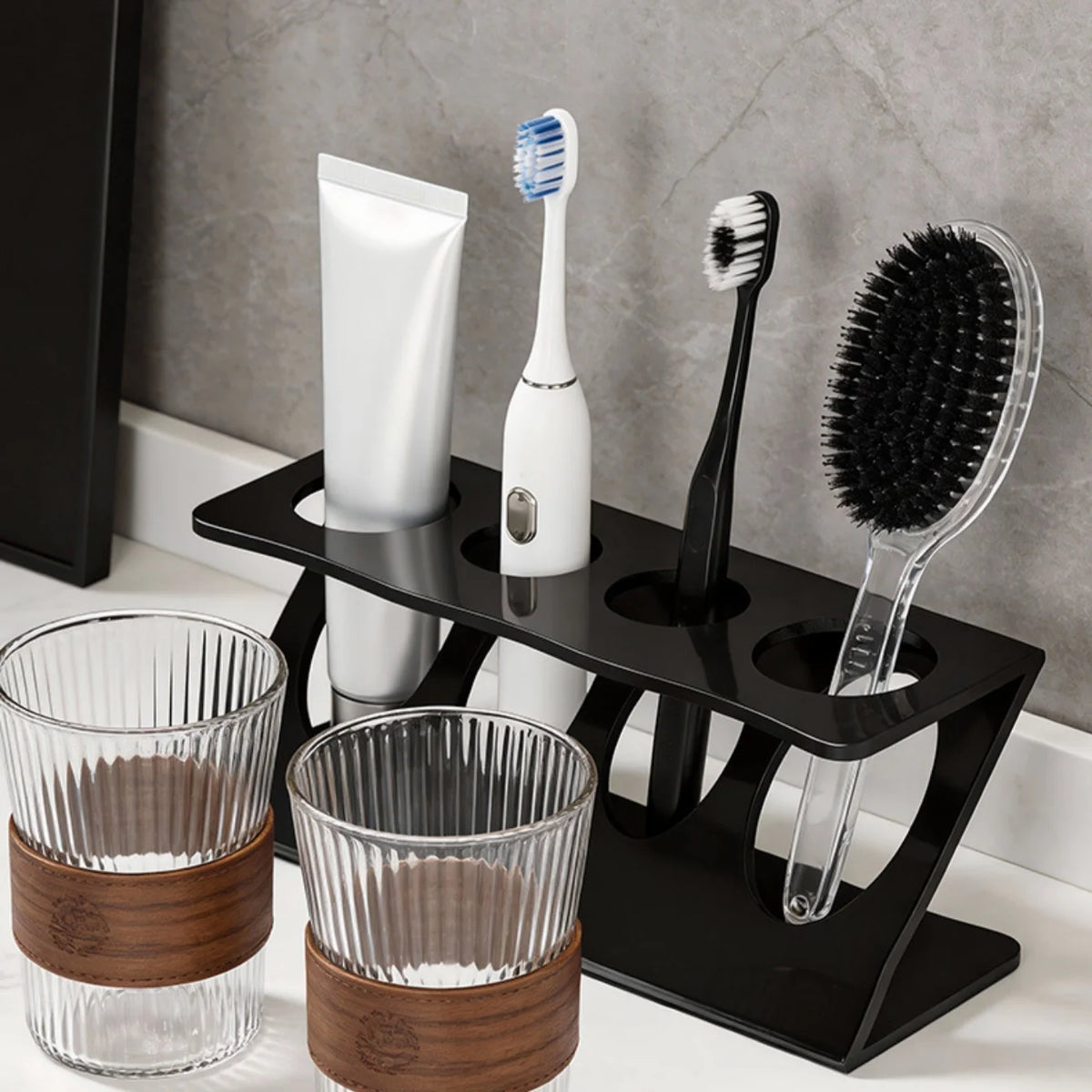 Black plastic ventilated toothbrush and toothpaste stand on bathroom counter holding brushes, toothpaste, and a small comb