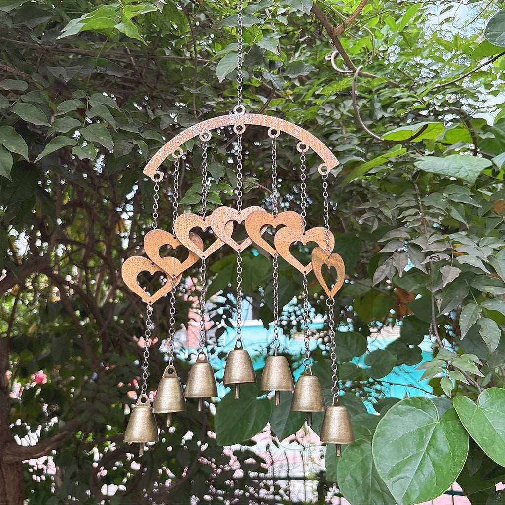 Decorative hanging wind chime with hearts and bells among garden greenery