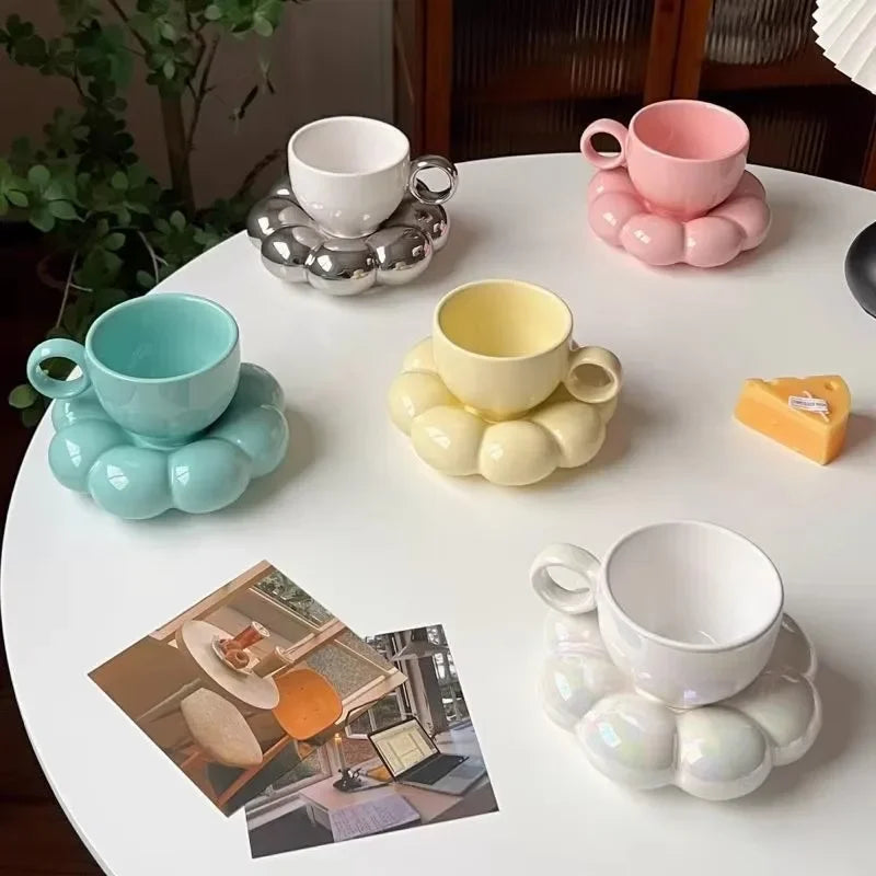 Five cloud ceramic mug and saucer sets in pastel colors arranged on a round white table