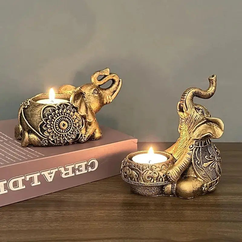 Two resin elephant tealight candle holders in gold color, displayed with lit candles on a book and table.