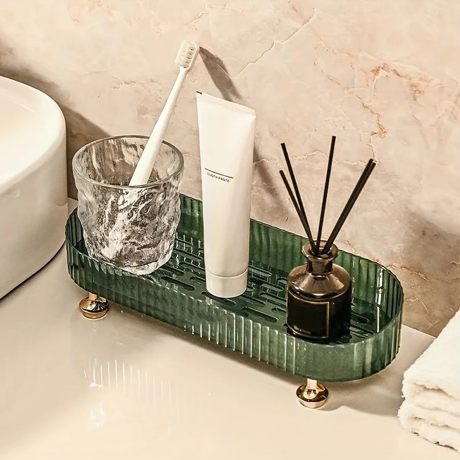Green acrylic vanity tray with gold feet holding a toothbrush cup, toothpaste, and a diffuser on a tidy bathroom counter