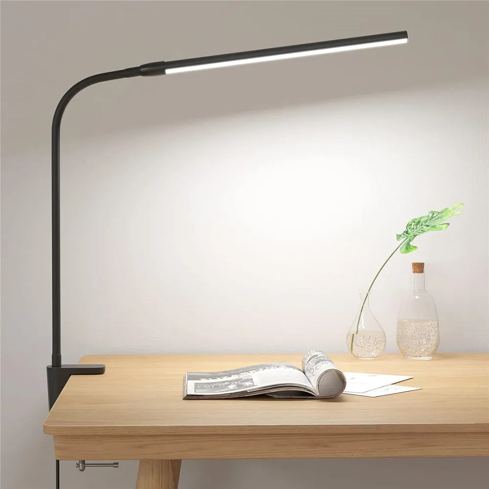Black clamp LED desk lamp illuminating a wooden desk with open book