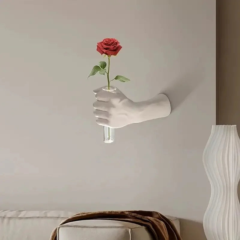 Fist-shaped wall vase with a single red rose on a beige living room wall