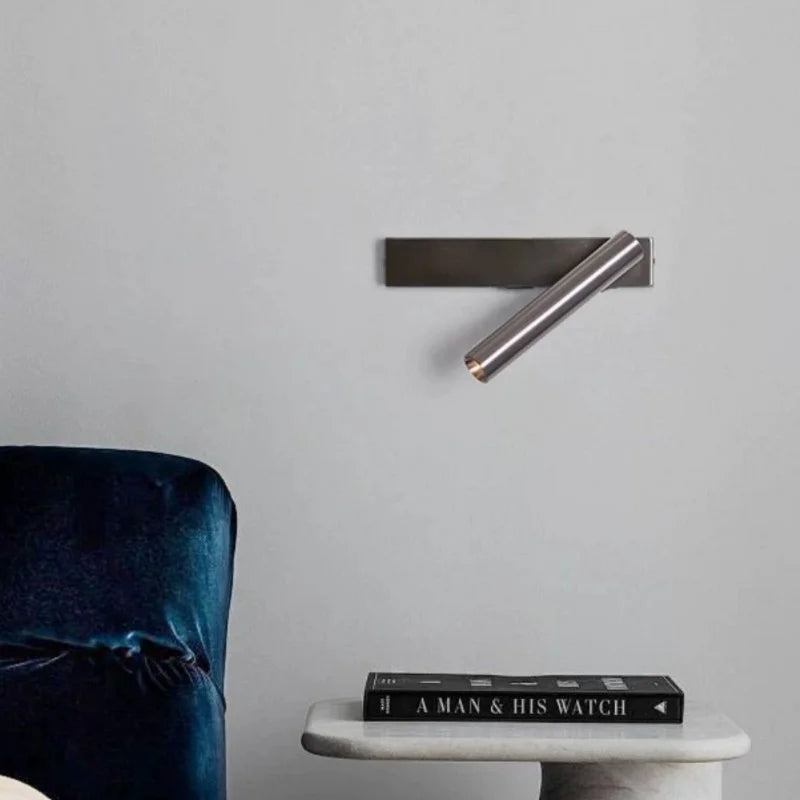 Minimalist rotating wall reading light in silver finish mounted above a small table in a bedroom setting
