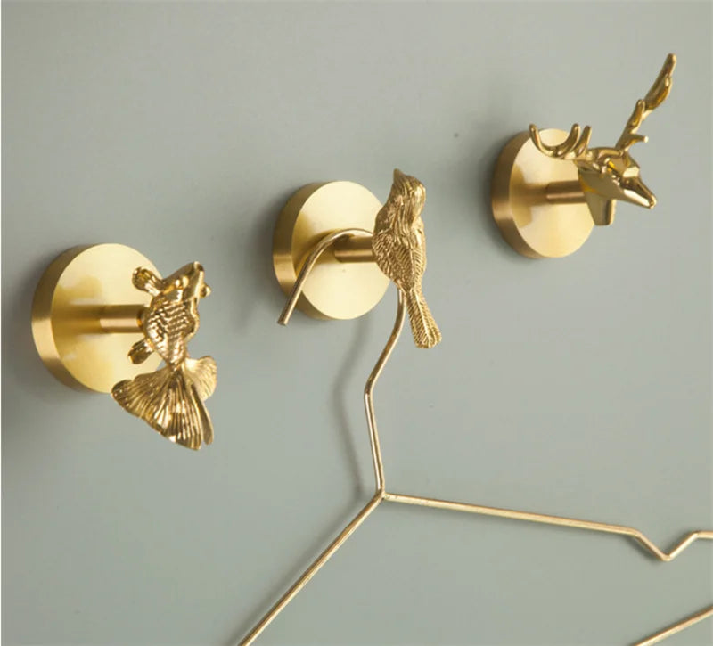 Brass bird, fish, and deer shaped wall hooks holding hangers