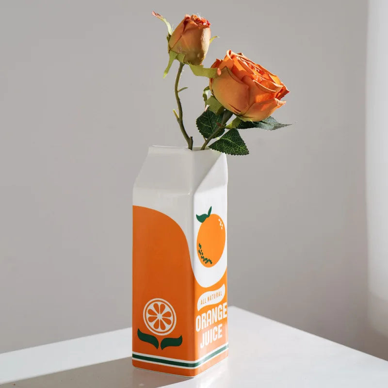 Side view of ceramic orange juice carton vase with orange roses in natural light