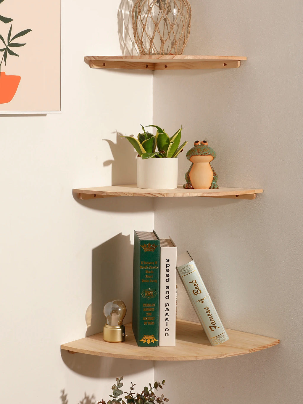 Close-up of two upper corner shelves showing books, a potted plant, and a ceramic frog on natural wood