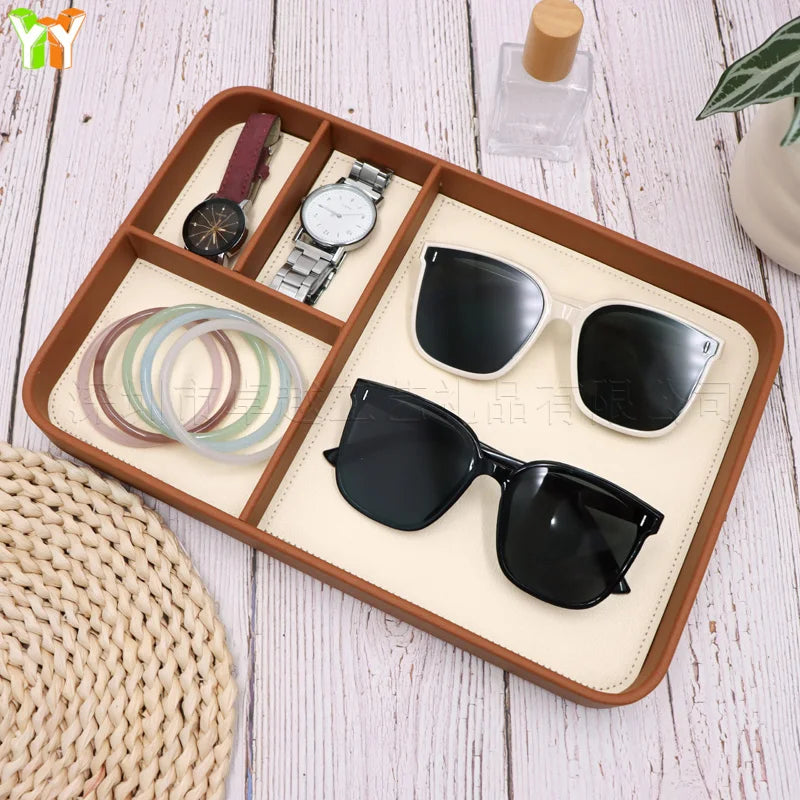 Wood compartment organizer tray holding sunglasses, watches, and bracelets on a white tabletop