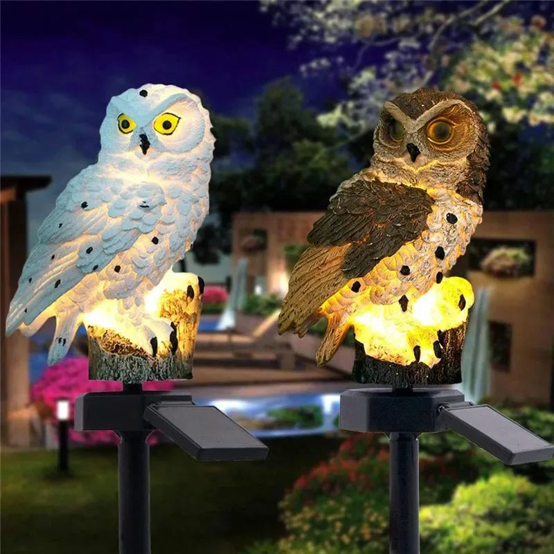 Two solar owl garden stake lights glowing at night in an outdoor garden setting