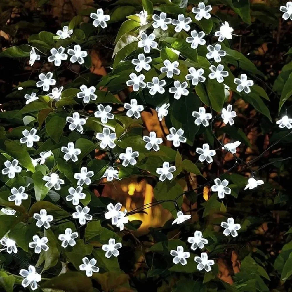 White blossom-shaped solar string lights on leafy outdoor foliage at dusk
