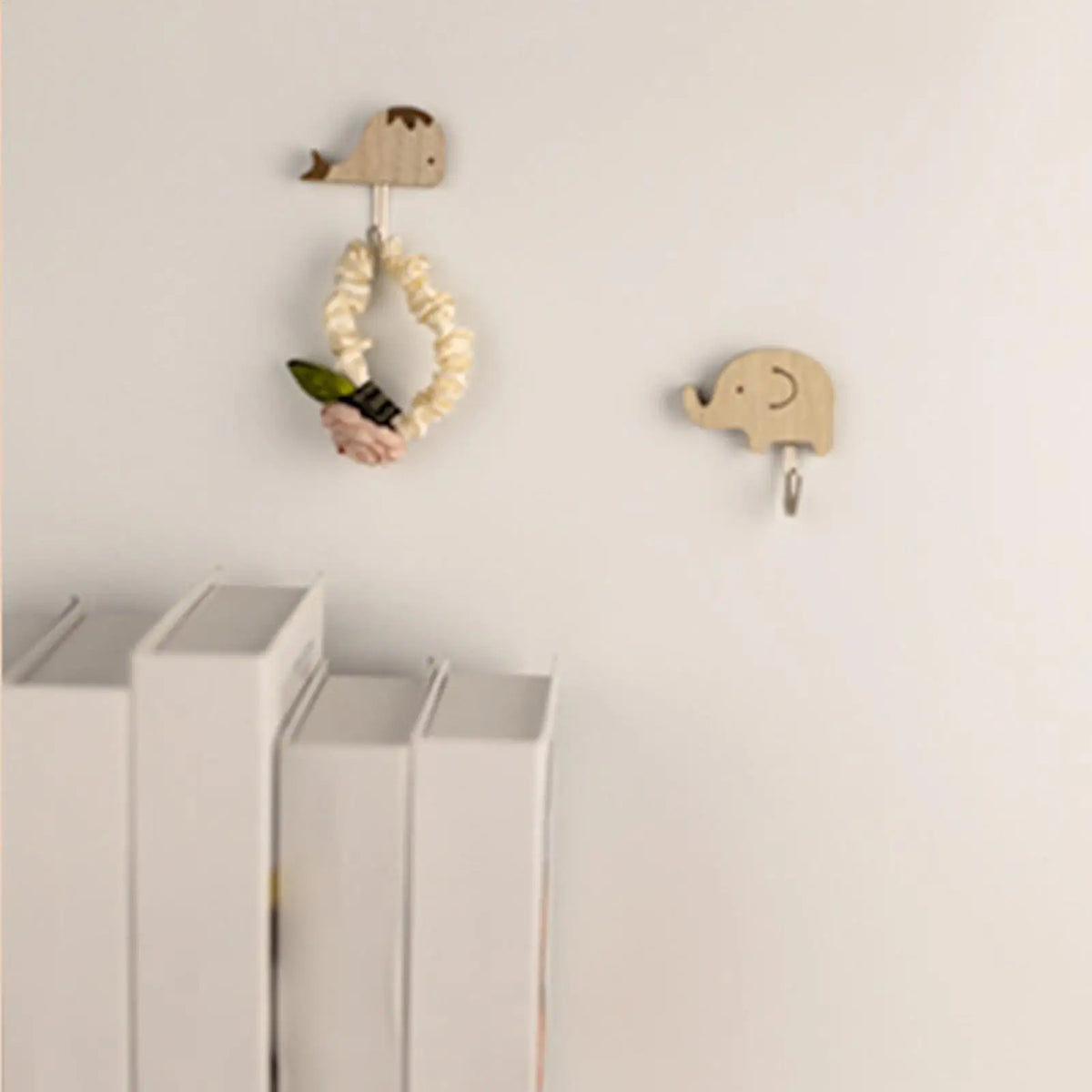 whale and elephant bamboo wall hooks on a white wall, one holding a scrunchie, next to a bookshelf