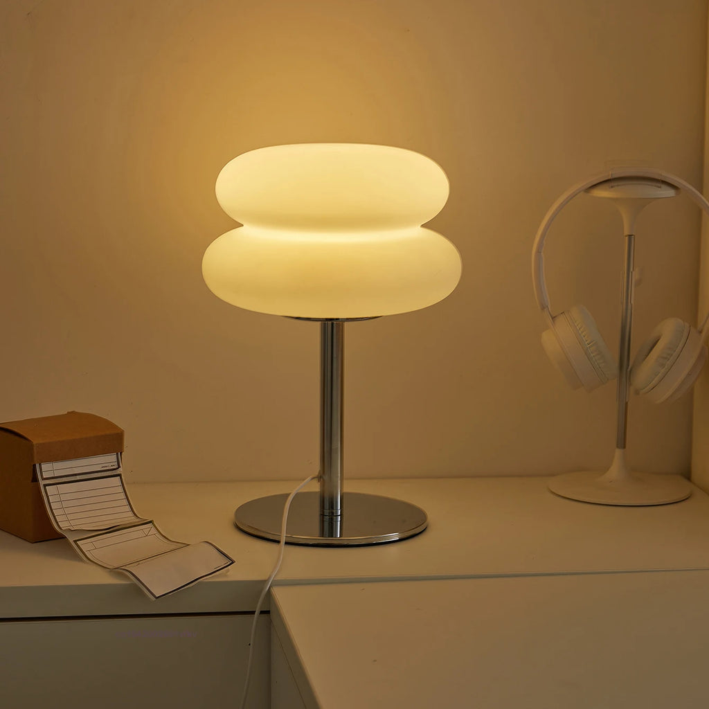 Cloud-shaped lamp on a desk with warm lighting, next to headphones and desk accessories