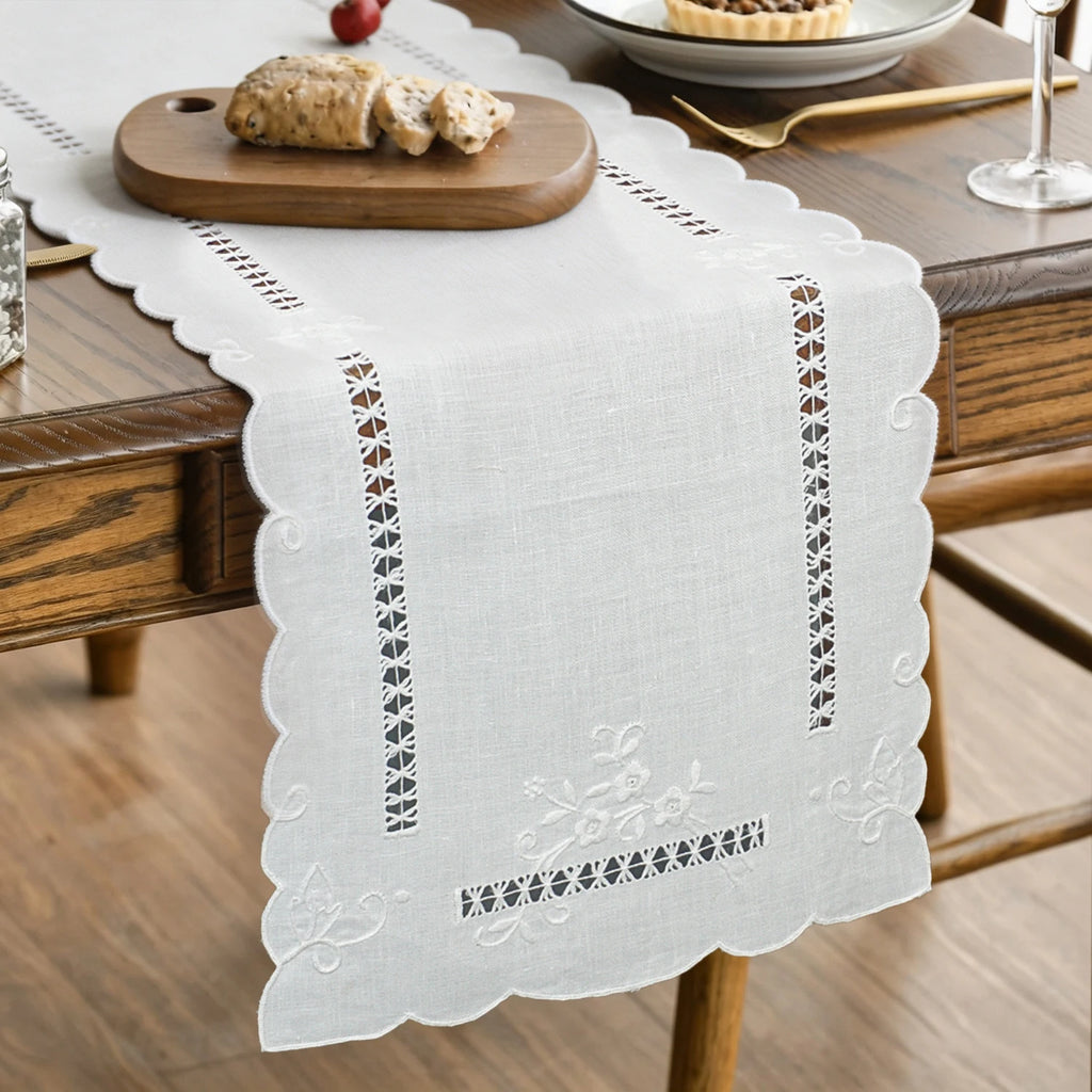 Hand-embroidered linen table runner with cutwork displayed on a rustic dining table