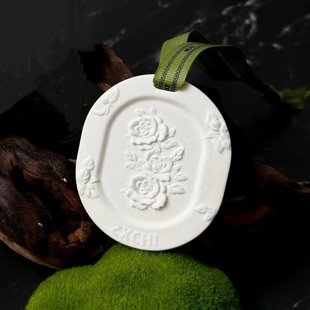 Side view of an embossed floral scented stone with ribbon, displayed on moss and driftwood