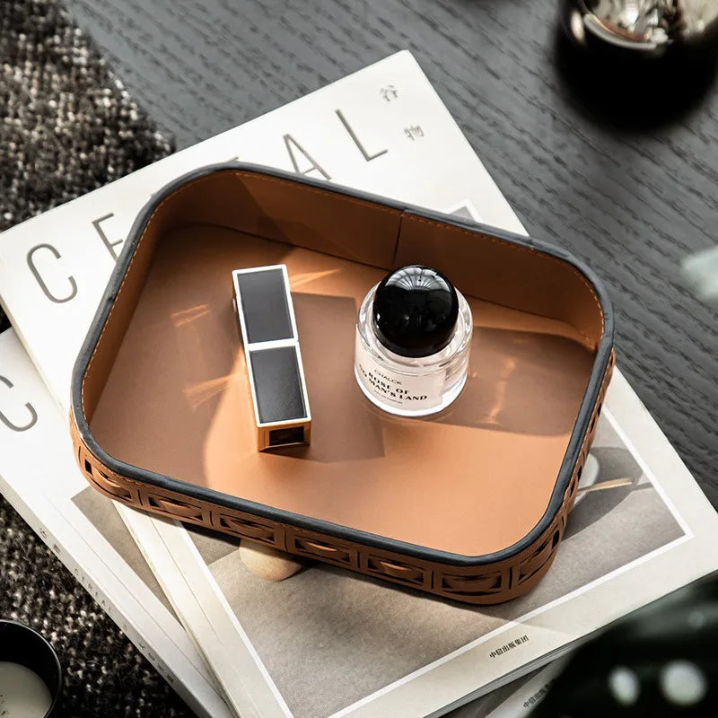 Brown leather desk organizer tray with perfume and lipstick on a stack of magazines