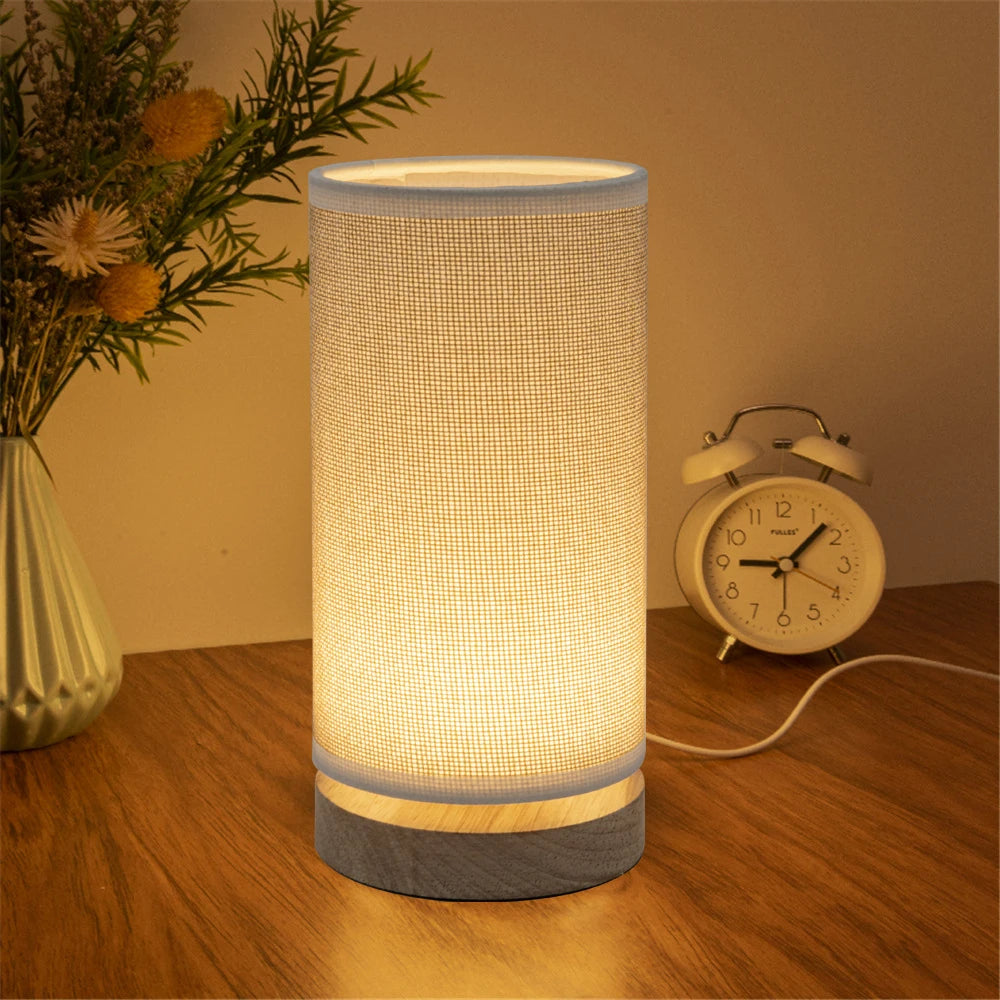 LED bedside lamp with linen shade and wood base on a desk near a vase and clock