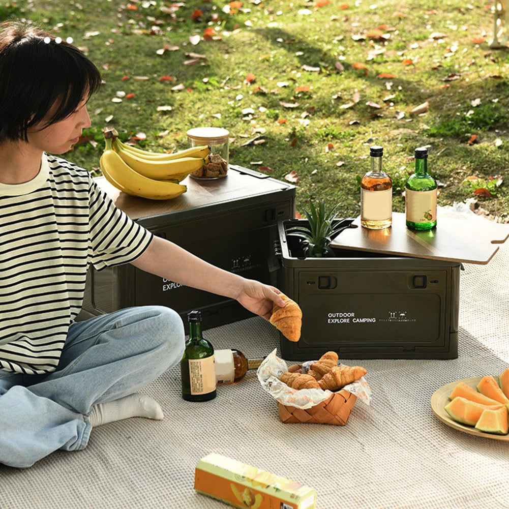 Person sitting outdoors with collapsible bins used as tables and storage on a picnic blanket