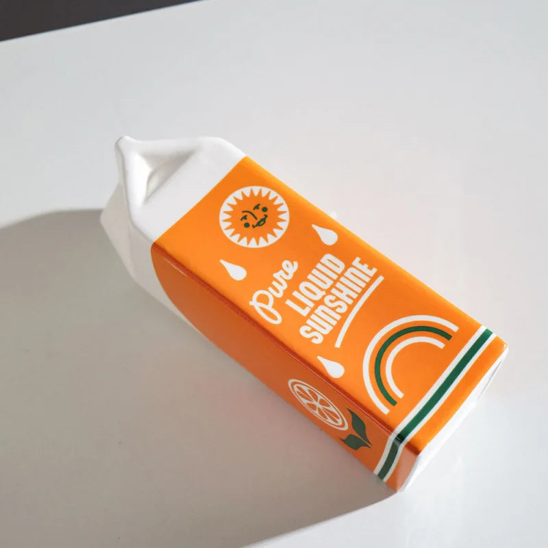 Bottom of orange juice carton ceramic vase showing 'Pure Liquid Sunshine' and rainbow graphic