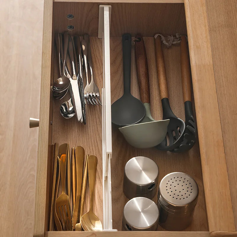 Single expandable divider separating utensils, ladles, and containers in a kitchen drawer