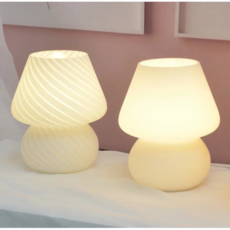 Two glass mushroom table lamps lit on a nightstand against a pink wall