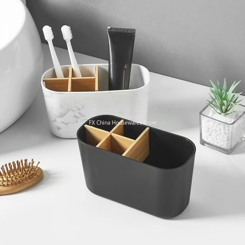 Black and marble toothbrush holders with bamboo dividers on a bathroom counter, one empty and one holding two toothbrushes and a toothpaste tube, with a hairbrush and decorative plant