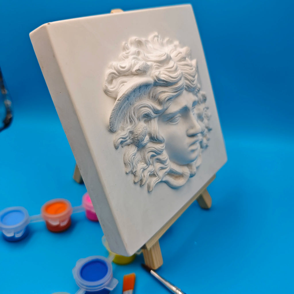 side perspective of plaster Medusa wall plaque with paint pots and brushes nearby