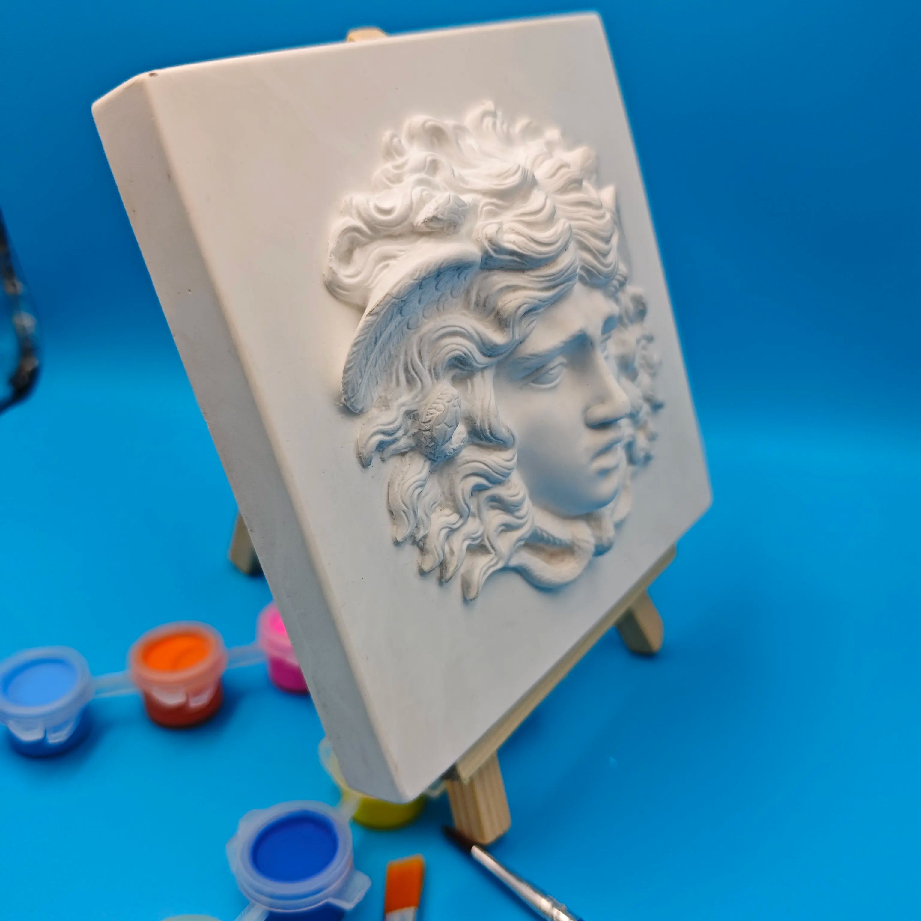side perspective of plaster Medusa wall plaque with paint pots and brushes nearby