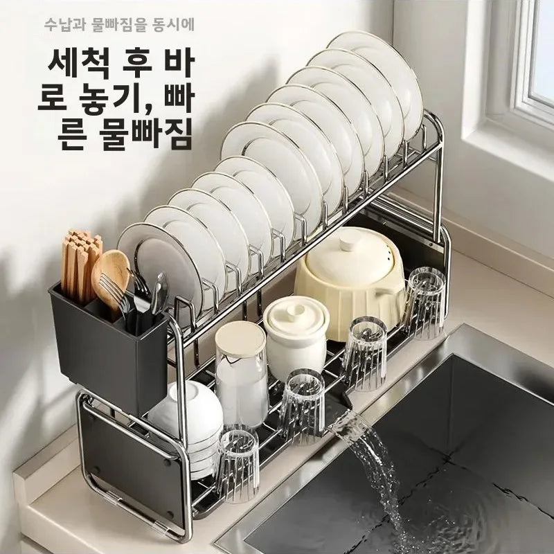 Two-tier narrow kitchen dish drying rack with plates, utensils, and cups beside a sink, water draining into sink
