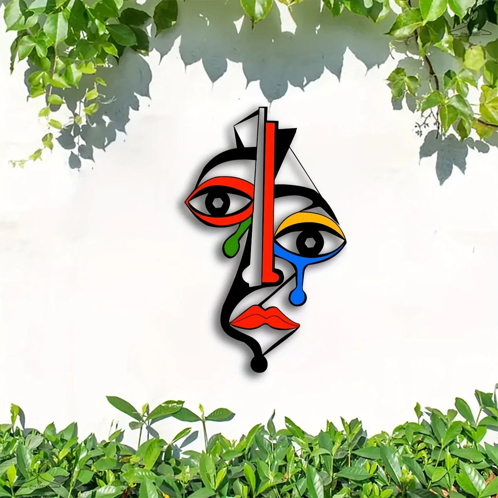 Artistic colorful metal face wall decor on a white wall with green foliage at the top
