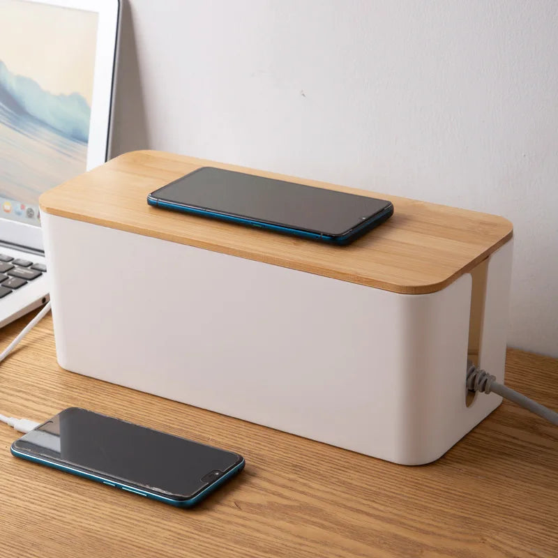 White cable management box with bamboo lid on a desk, phone charging on top