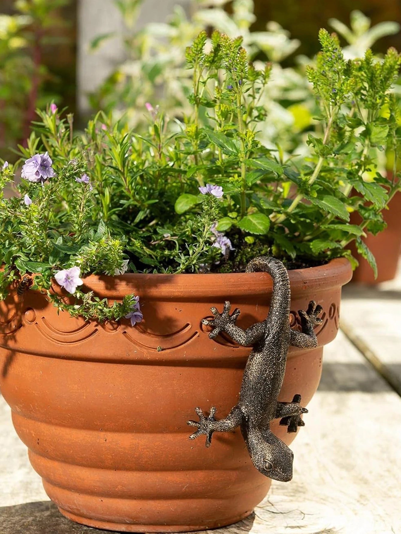 Brown resin gecko ornament perched on a large outdoor planter with green plants