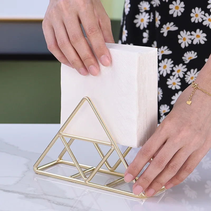 Gold geometric triangle metal napkin holder with napkins on a marble countertop