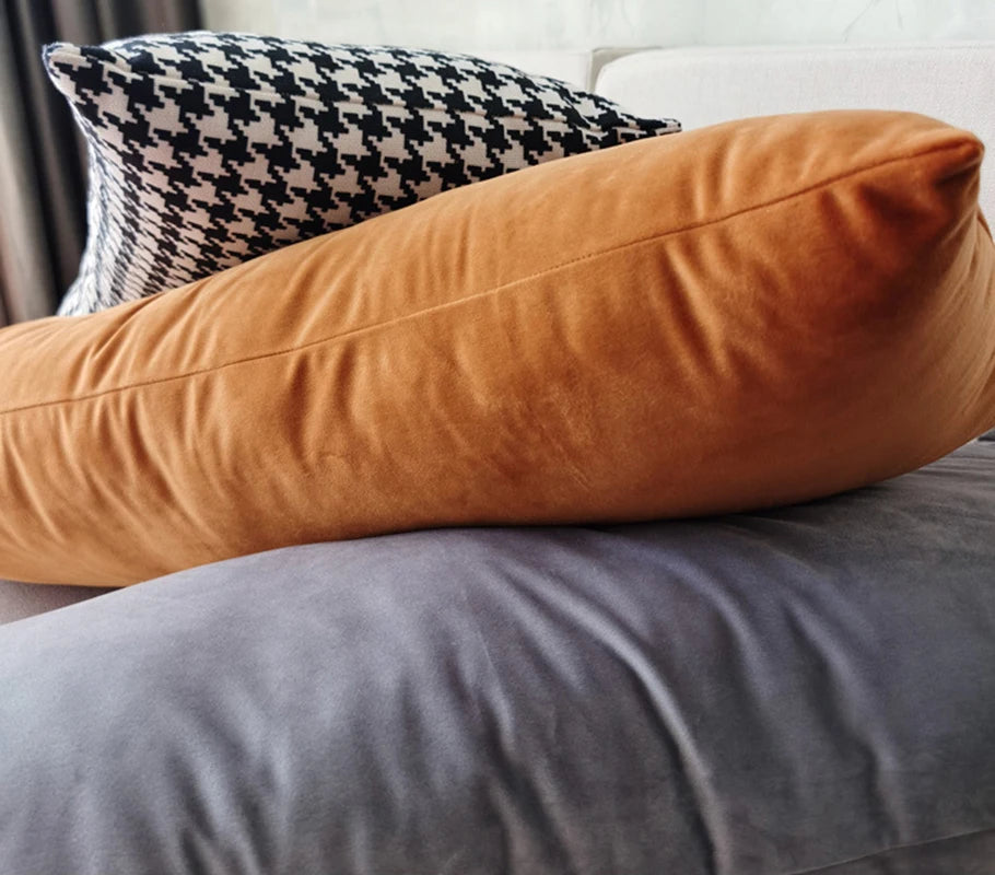 Close-up of rectangular orange velvet, gray velvet, and houndstooth pillow covers on a sofa