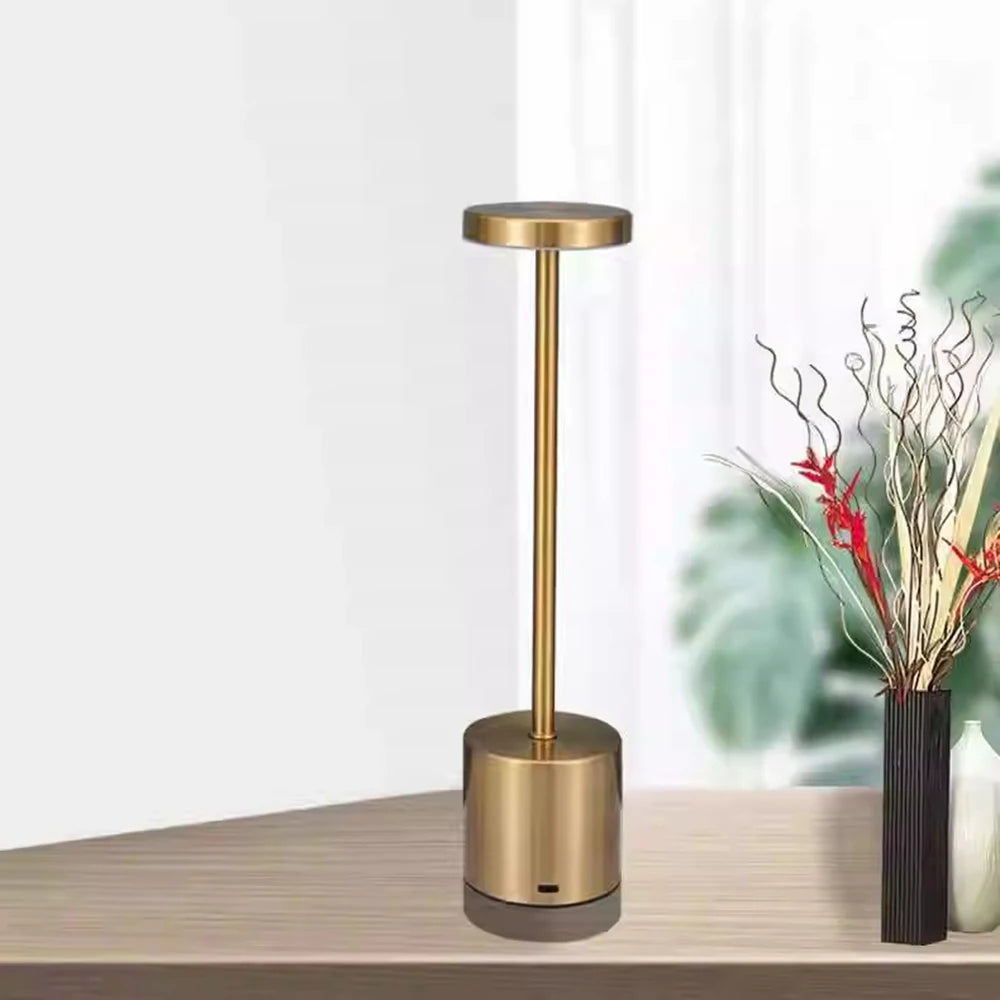 Gold rechargeable touch table lamp on a wood surface beside a vase
