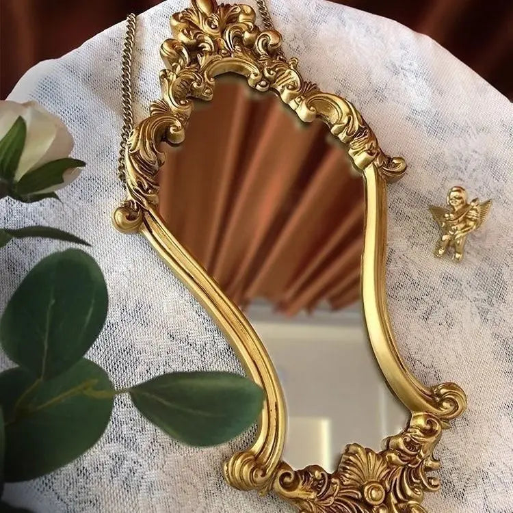 Ornate gold vintage wall mirror resting on a lace cloth with greenery