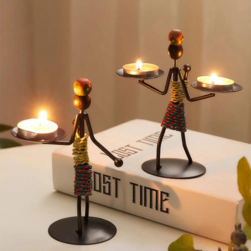 Two abstract character candlestick figures in colorful cord wraps holding tealight trays, with lit tealight candles