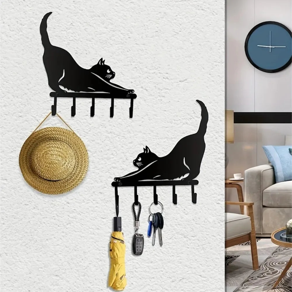 Two black metal cat-shaped wall key holders with keys, umbrella, and hat hanging in a home entryway