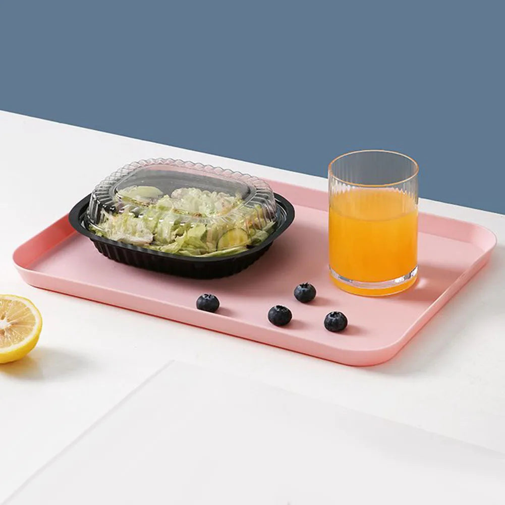Pink matte plastic tray serving salad and orange juice on a table with blueberries and a lemon slice.